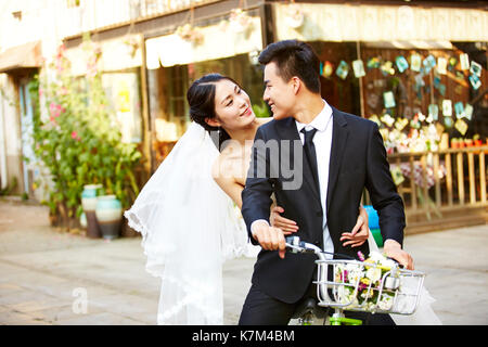 romantic asian newly wed couple having fun riding a bicycle together. Stock Photo