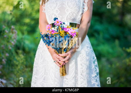 Bride holding colorful bouquet in the forest outdoors Stock Photo