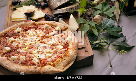 Pizza on board, cheese and leafs on the table Stock Photo
