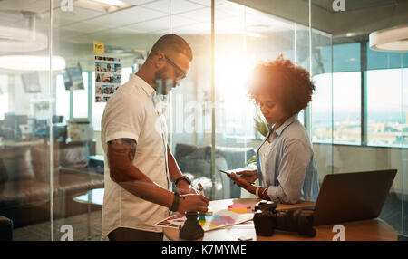 Two young photographers discussing shooting plan at creative workplace. Design professionals working together in modern office. Stock Photo