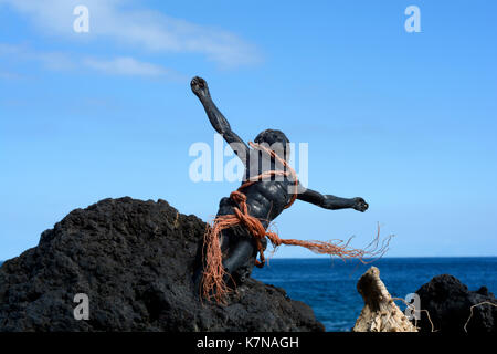 Photo of a Jesus figurine bound in rope and  embedded in volcanic rock on the coast of Tenerife Stock Photo