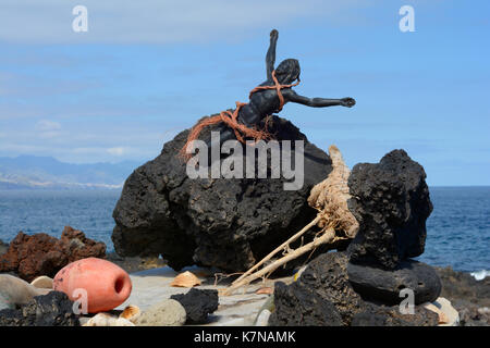 Photo of a Jesus figurine bound in rope and  embedded in volcanic rock on the coast of Tenerife Stock Photo