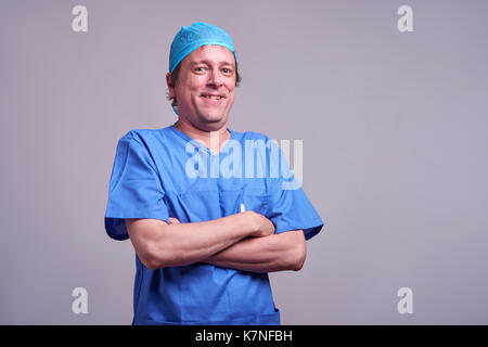 A happy middle aged male doctor standing in blue scrubs and laughing Stock Photo