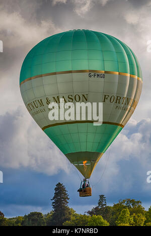 Fortnum & Mason hot air balloon in the sky and clouds above trees at Sky Safari hot air balloons festival at Longleat, Wiltshire UK - hdr effect Stock Photo