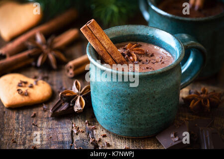 Hot chocolate with a cinnamon stick, anise star and grated chocolate topping in festive Christmas setting on dark rustic wooden background Stock Photo