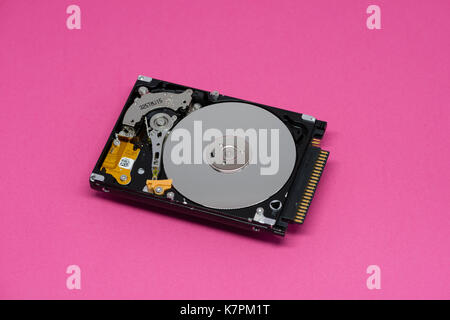 Close-up of an opened computer hard drive disk on mauve colored background. Read-write head retracted. Stock Photo