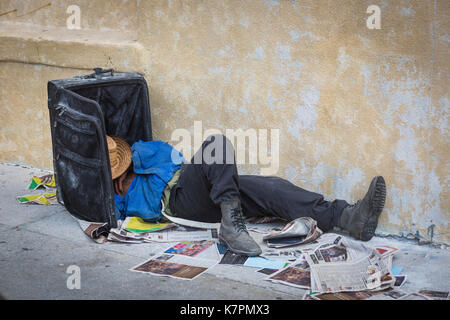 Reclining man with head in suitcase, presumably homeless, in Downtown, Los Angeles, in the Fashion District, near Skid Row. Stock Photo