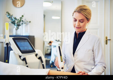 Focused young female beautician performing electrolysis on the legs of a woman lying on a table in a beauty clinic Stock Photo