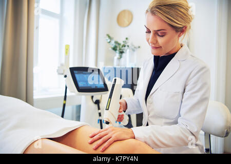 Focused female beautician performing electrolysis on the legs of a woman lying on a table in a beauty clinic Stock Photo