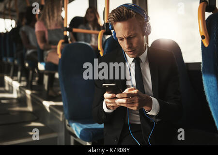 Focused young businessman wearing a suit listening to music and reading text messages while sitting on a bus during his morning commute Stock Photo