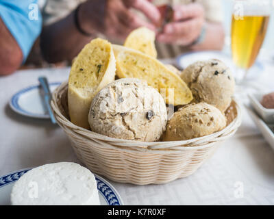 bread basket on a table with a selection of bread. Olive bread rolls and garlic bread baguette sliced. Goats cheese is also on the table and a glass o Stock Photo
