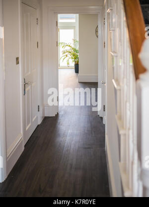 natural daylight illuminating the laminate wood flooring of a hall way in a residential home interior. The walls are white, the banister and stair cas Stock Photo