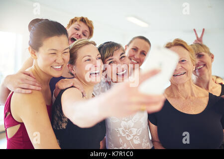 Laughing group of senior women standing arm in arm together taking a selfie with their dance teacher during ballet class Stock Photo