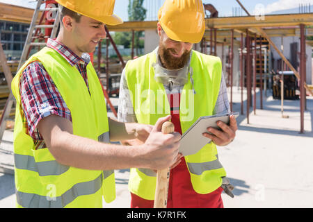 Two young construction workers smiling while using a tablet duri Stock Photo