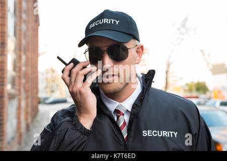 Portrait Of Young Male Security Guard Talking On Walkie-talkie Stock Photo