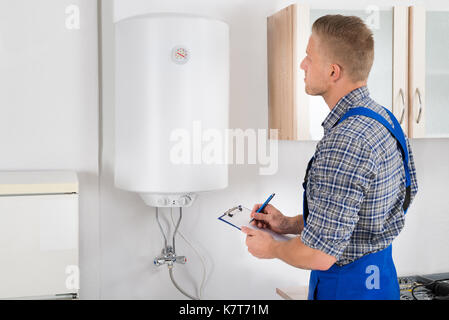 Young Man Writing On Clipboard While Looking At Electric Boiler Stock Photo