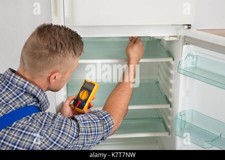Young Male Technician Checking Fridge With Digital Multimeter Stock Photo