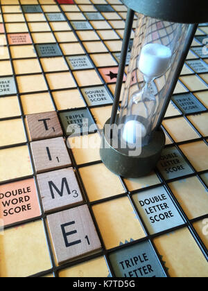 The word 'time' spelled out on a Scrabble game board, next to an hourglass Stock Photo