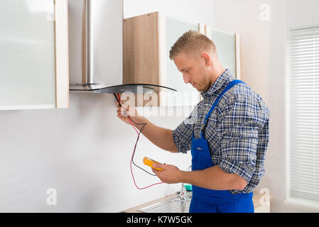 Male Worker In Overall Testing Kitchen Hood With Multimeter In Hands Stock Photo