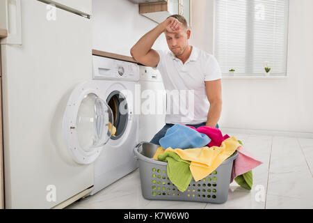 Tired Young Man Loading Clothes Into The Washing Machine At Home Stock Photo