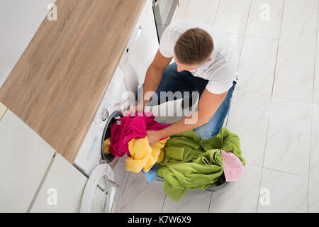High Angle View Of Young Man Putting Clothes In Washing Machine Stock Photo