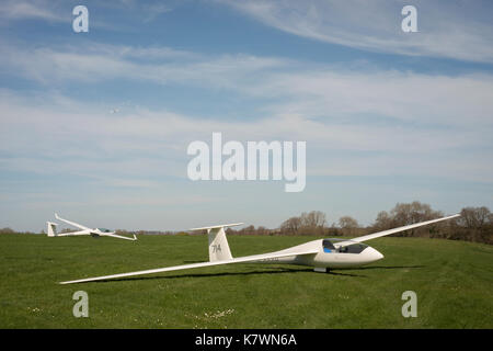 Two gliders on the ground with a third glider being towed in the air by a tow plane. Storrington, West Sussex, United Kingdom Stock Photo