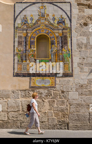 Old town Valencia, a woman traveller walks past a colourful tiled plaque set in the wall of the Santa Catalina church in the centre of Valencia, Spain. Stock Photo