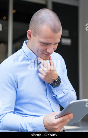 Handsome young businessman is using a digital tablet and smiling while resting outdoors Stock Photo