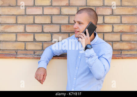 Portrait of a handsome young man outside while talking on a mobile phone. Behind him is a wall of old brick. Copy space Stock Photo