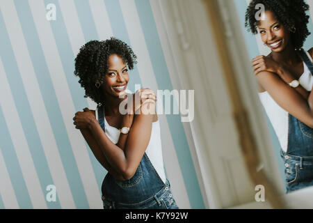 Pretty African American woman posing in jeans trousers by the wall in the room Stock Photo
