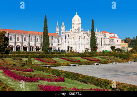 View of urban park with flowers and Jeronimos (aka Hieronymites) Monastery under blue sky in Lisbon, Portugal. Stock Photo