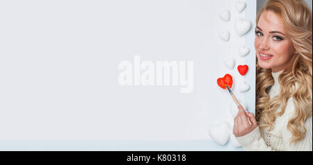 Young happy woman painting in red decorative hearts, Valentines day concept Stock Photo