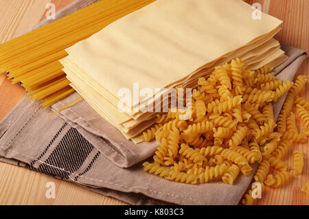 Assorted types of pasta on wooden background. Various forms of pasta, spaghetti, lasagna sheets and fusilli. Stock Photo