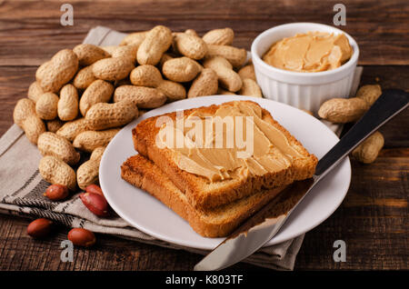 Peanut butter sandwich on plate with inshell peanuts, breakfast on the wooden background Stock Photo
