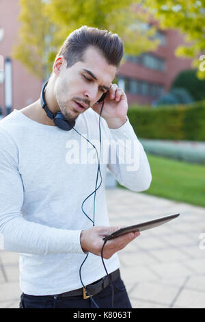 Young man listening music on tablet by hadphones outdoor Stock Photo