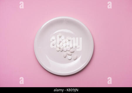 Pills served as a healthy meal. Drug capsule on white plate on pink background Stock Photo