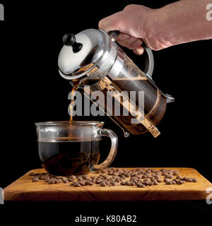Coffee press made of glass moves coffee into a cup with beens on a table Stock Photo