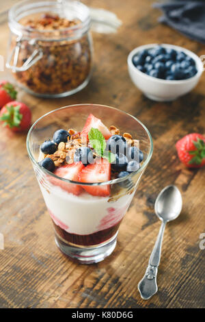 Yogurt with granola, blueberries and strawberies in glass on wooden table. Healthy snack, healthy breakfast