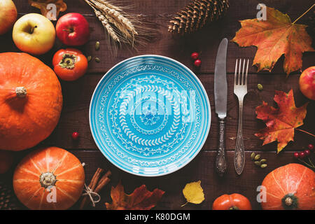 Autumn Halloween or thanksgiving day table setting. Fallen leaves, pumpkins, spices, empty plate and vintage cutlery on wooden table. Top view, toned  Stock Photo