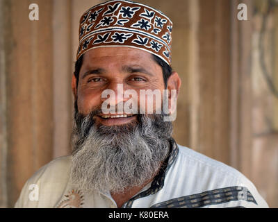 Indian Muslim man with Muslim-style trimmed full beard wears an Omani-style patterned Islamic prayer cap (taqiyah) and smiles for the camera. Stock Photo