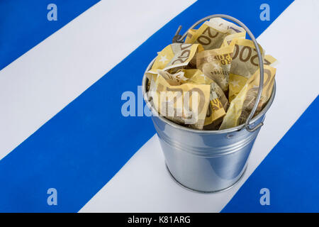 Greek flag with a metal bucket of 200 Euro banknotes. For Greek financial crisis & bailout, Greek debt relief, Greece economic slump, Greek recession. Stock Photo
