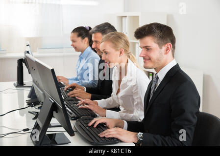 Group Of Businesspeople Typing On Desktop Computer At Desk Stock Photo