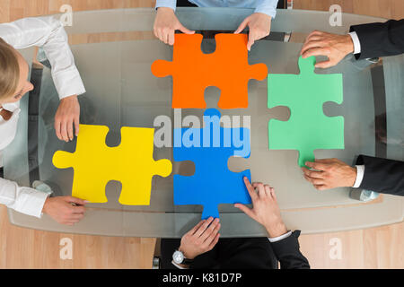 High Angle View Of Businesspeople With Multi-colored Jigsaw Pieces At Desk Stock Photo