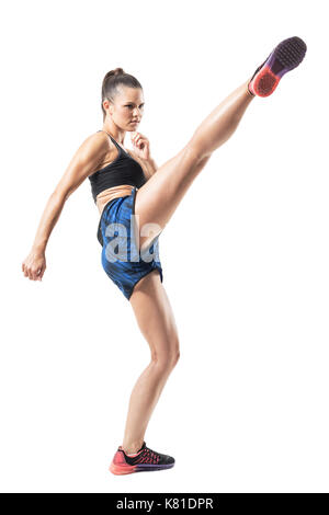 Stopped action motion of tough woman kickboxing fighter doing high kick. Full body length portrait isolated on white studio background. Stock Photo