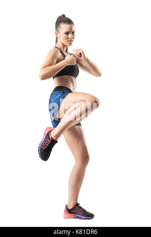 Focused female mma fighter kicking with leg. Stopped action motion. Full body length portrait isolated on white studio background. Stock Photo