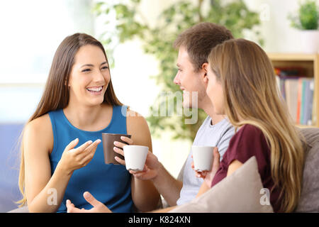 Three happy friends talking and drinking coffee sitting on a couch at home Stock Photo