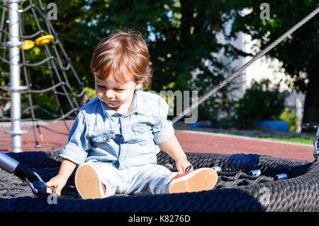 Playful boy sitting on a round swing in the park Stock Photo
