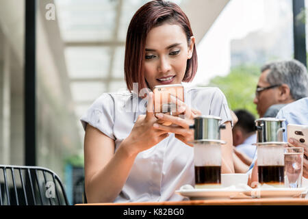 Portrait of a young Asian woman using a mobile phone at a coffee Stock Photo