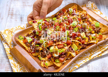 Mexican nacho yellow corn tortilla chips with cheese, meat, avocado guacamole and red salsa Stock Photo
