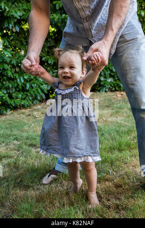 Father helping his nine month old girl to walk in her yard.  She loves to try to walk! Stock Photo
